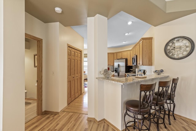 kitchen featuring kitchen peninsula, light hardwood / wood-style flooring, stainless steel appliances, a breakfast bar, and light stone countertops