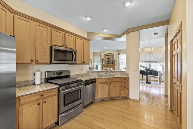 kitchen with a notable chandelier, stainless steel appliances, light hardwood / wood-style floors, and a textured ceiling