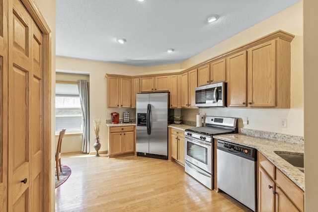 kitchen featuring light wood-type flooring, sink, stainless steel appliances, light stone countertops, and a textured ceiling