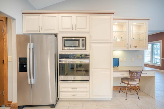 kitchen with cream cabinets, light tile patterned floors, lofted ceiling, and appliances with stainless steel finishes