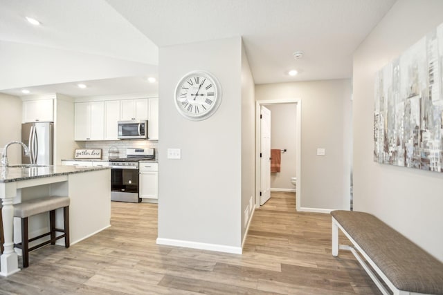 kitchen with light wood-type flooring, light stone counters, stainless steel appliances, and white cabinets