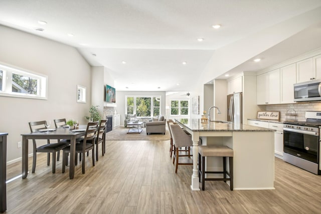 kitchen with appliances with stainless steel finishes, plenty of natural light, vaulted ceiling, and an island with sink