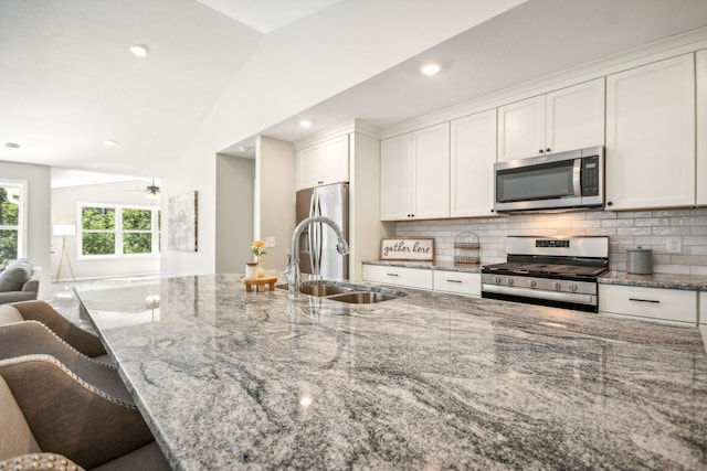 kitchen featuring light stone counters, sink, vaulted ceiling, appliances with stainless steel finishes, and a kitchen bar