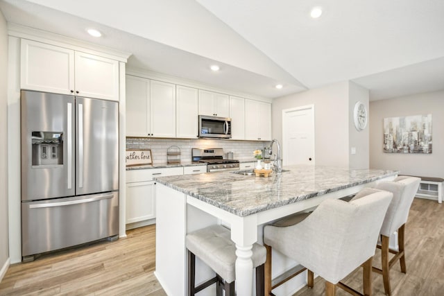 kitchen with stainless steel appliances, a center island with sink, light stone counters, and white cabinetry