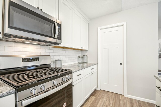 kitchen featuring light stone counters, stainless steel appliances, light wood-type flooring, and white cabinetry