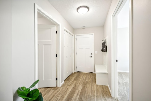 corridor with a textured ceiling and light wood-type flooring