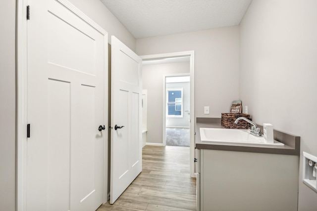 laundry area with sink, light wood-type flooring, and a textured ceiling