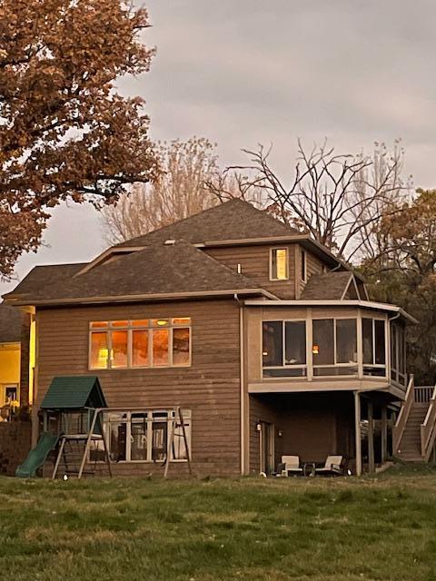 rear view of house with a playground, a sunroom, and a yard