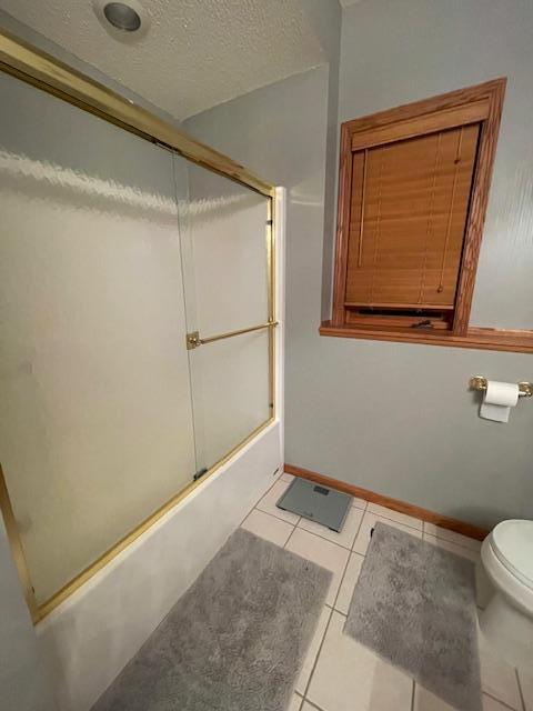 bathroom with toilet, shower / bath combination with glass door, a textured ceiling, and tile patterned floors