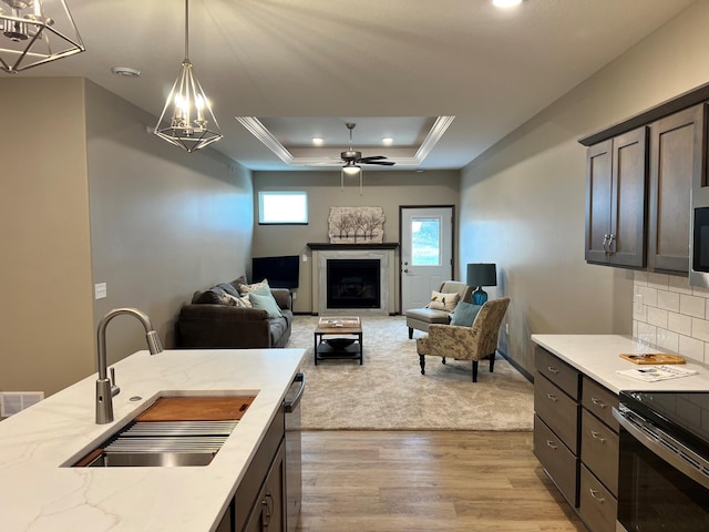 kitchen with a raised ceiling, sink, light hardwood / wood-style floors, dark brown cabinets, and decorative light fixtures