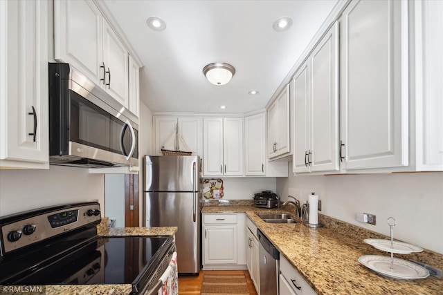 kitchen with sink, light stone countertops, white cabinets, appliances with stainless steel finishes, and light hardwood / wood-style floors