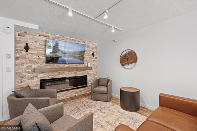 living room with a textured ceiling, track lighting, a fireplace, and wood-type flooring