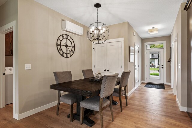 dining space featuring light hardwood / wood-style floors, a wall mounted air conditioner, washer / clothes dryer, and a chandelier