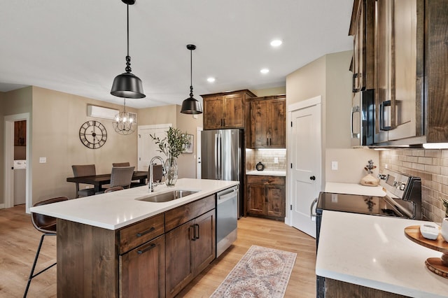 kitchen with light wood-type flooring, stainless steel appliances, sink, a center island with sink, and decorative light fixtures