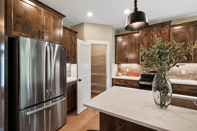 kitchen featuring light stone countertops, decorative backsplash, light hardwood / wood-style floors, hanging light fixtures, and appliances with stainless steel finishes