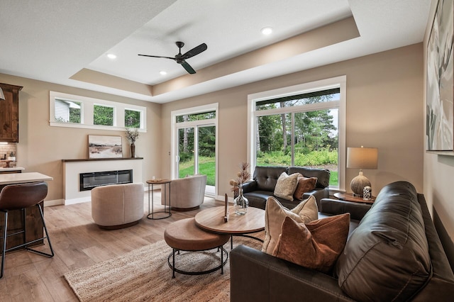 living room featuring ceiling fan, plenty of natural light, light hardwood / wood-style flooring, and a raised ceiling