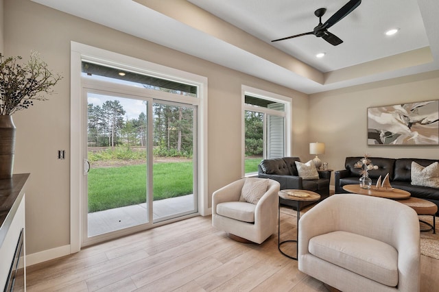 living room with ceiling fan, a raised ceiling, and light hardwood / wood-style flooring