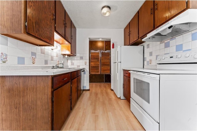 kitchen featuring light wood-type flooring, white appliances, sink, backsplash, and a textured ceiling