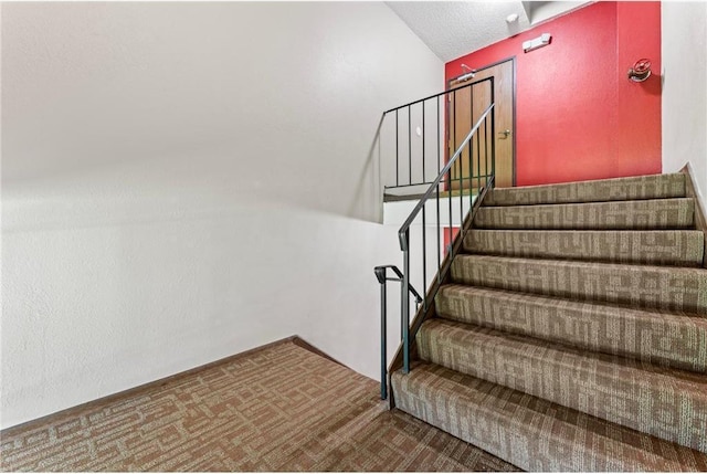 stairs with lofted ceiling, carpet, and a textured ceiling