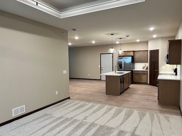 kitchen featuring an island with sink, light wood-type flooring, decorative light fixtures, and appliances with stainless steel finishes