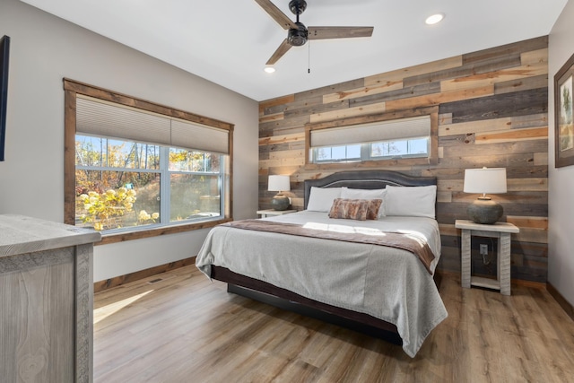 bedroom with ceiling fan, wood walls, and light wood-type flooring