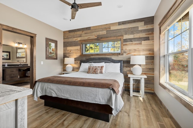 bedroom featuring ensuite bath, wooden walls, light hardwood / wood-style floors, and ceiling fan