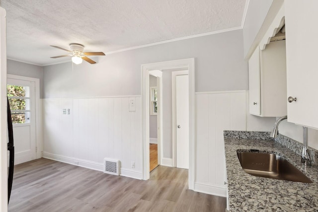 kitchen featuring dark stone counters, white cabinets, sink, ornamental molding, and a textured ceiling