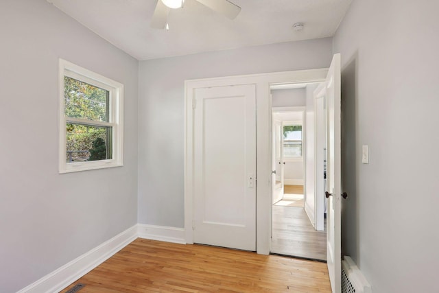 unfurnished bedroom featuring ceiling fan, a baseboard heating unit, a closet, and light hardwood / wood-style flooring