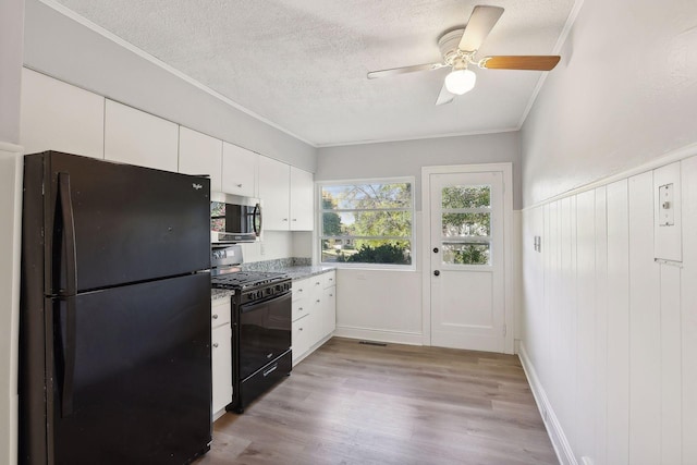 kitchen with light wood-type flooring, white cabinetry, crown molding, and black appliances