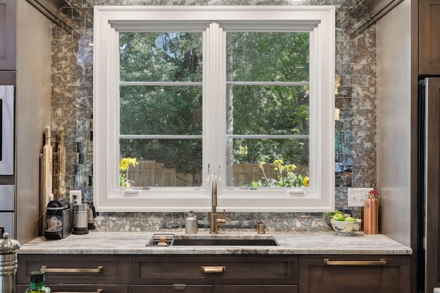 bar with dark brown cabinets, stainless steel refrigerator, a wealth of natural light, and sink