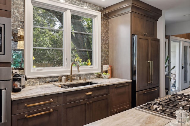 kitchen with built in fridge, plenty of natural light, light stone countertops, and sink