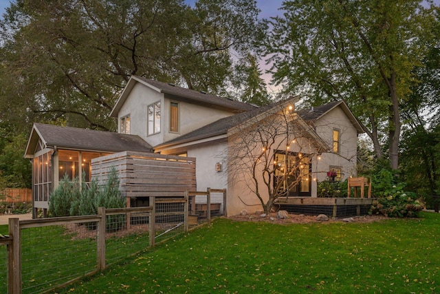 back house at dusk with a sunroom and a yard