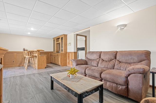 living room with bar area, a drop ceiling, and light hardwood / wood-style floors