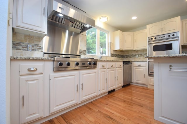 kitchen featuring decorative backsplash, light hardwood / wood-style flooring, range hood, stainless steel appliances, and white cabinetry