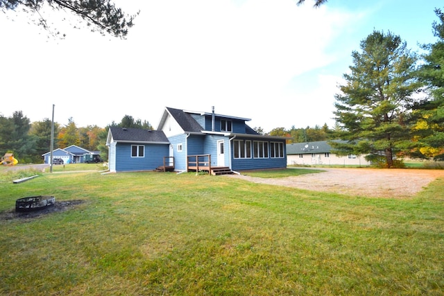 back of property with dirt driveway, a lawn, an outdoor fire pit, and a sunroom