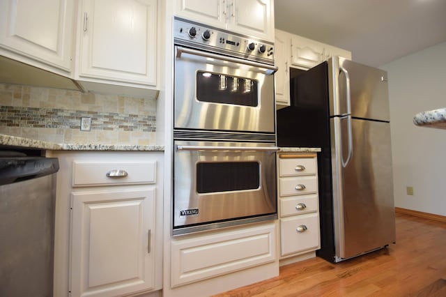 kitchen with light stone counters, light wood finished floors, appliances with stainless steel finishes, white cabinetry, and tasteful backsplash