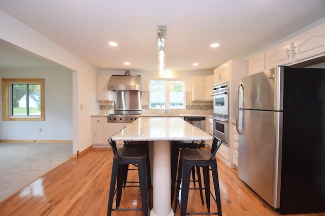 kitchen with ventilation hood, light stone counters, stainless steel appliances, a kitchen breakfast bar, and backsplash