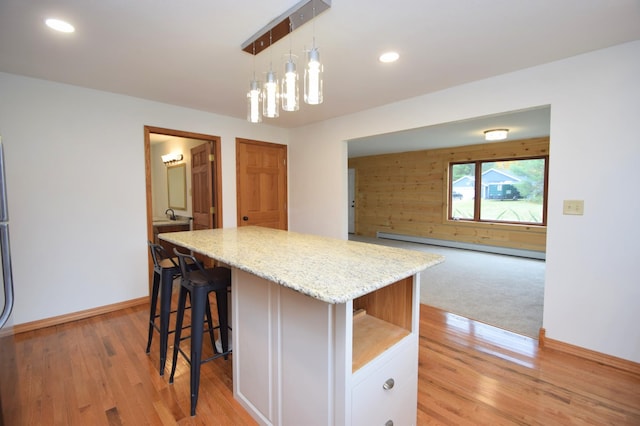 kitchen featuring a center island, light stone countertops, light wood-type flooring, a kitchen breakfast bar, and white cabinetry