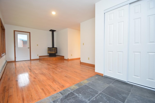 unfurnished living room featuring hardwood / wood-style flooring, a wood stove, and baseboards