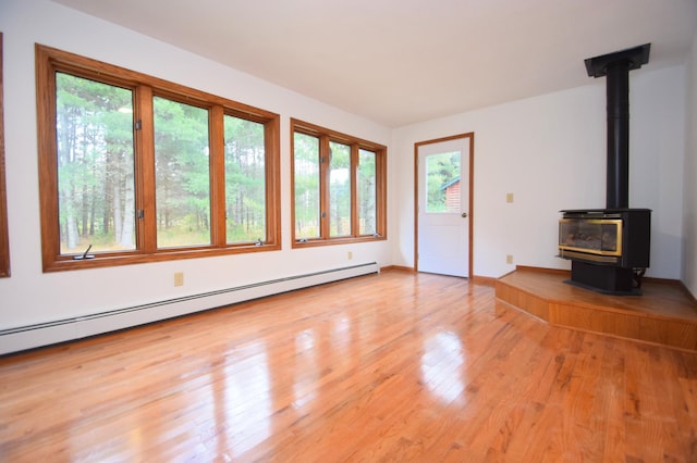 unfurnished living room with a baseboard radiator, baseboards, a wood stove, and light wood finished floors