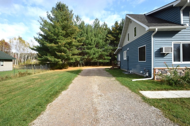 view of property exterior featuring a wall unit AC, fence, driveway, roof with shingles, and a lawn