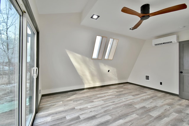 unfurnished room with lofted ceiling with skylight, a wall mounted AC, light wood-type flooring, and ceiling fan