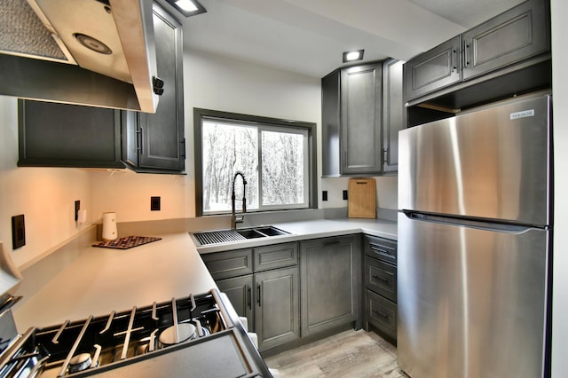 kitchen featuring sink, gas range oven, stainless steel refrigerator, light hardwood / wood-style flooring, and exhaust hood