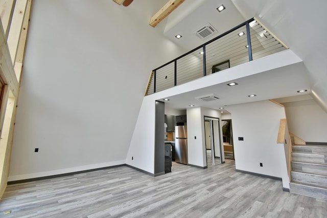 unfurnished living room featuring a towering ceiling and light hardwood / wood-style floors