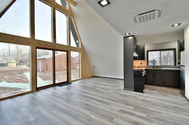 unfurnished living room featuring light hardwood / wood-style floors, a healthy amount of sunlight, sink, and a high ceiling