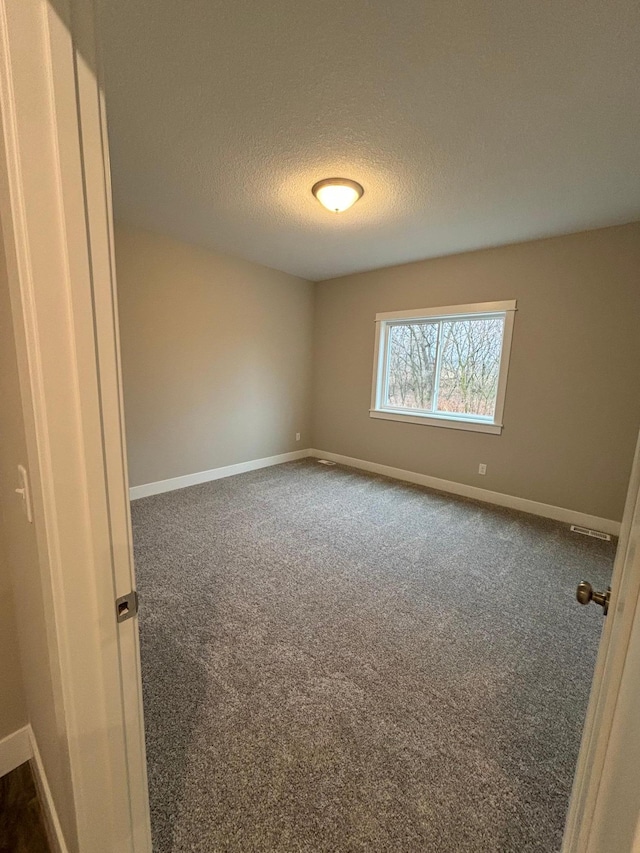 unfurnished room with dark carpet and a textured ceiling