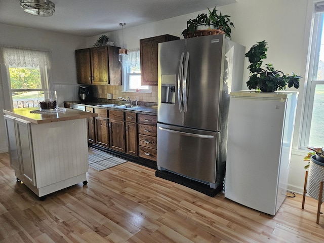 kitchen with light hardwood / wood-style flooring, stainless steel fridge with ice dispenser, white refrigerator, and hanging light fixtures