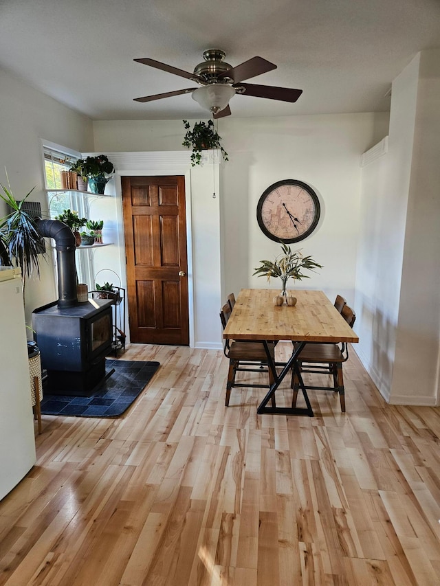 dining area with light hardwood / wood-style floors, a wood stove, and ceiling fan