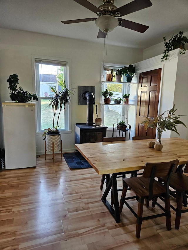 dining room featuring a wood stove, light wood-type flooring, and ceiling fan