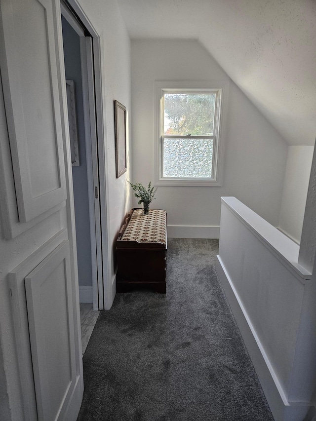 hallway featuring vaulted ceiling and dark carpet